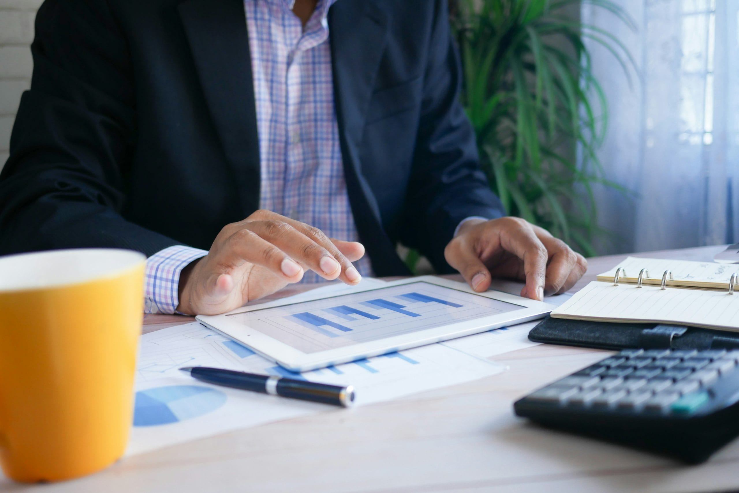 Um empresário do mercado financeiro usando um tablet em sua mesa verificando relatórios de gestão de riscos e compliance.