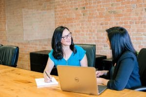 Soft skills para compliance officers, duas mulheres conversando em uma mesa em uma sala de reuniões